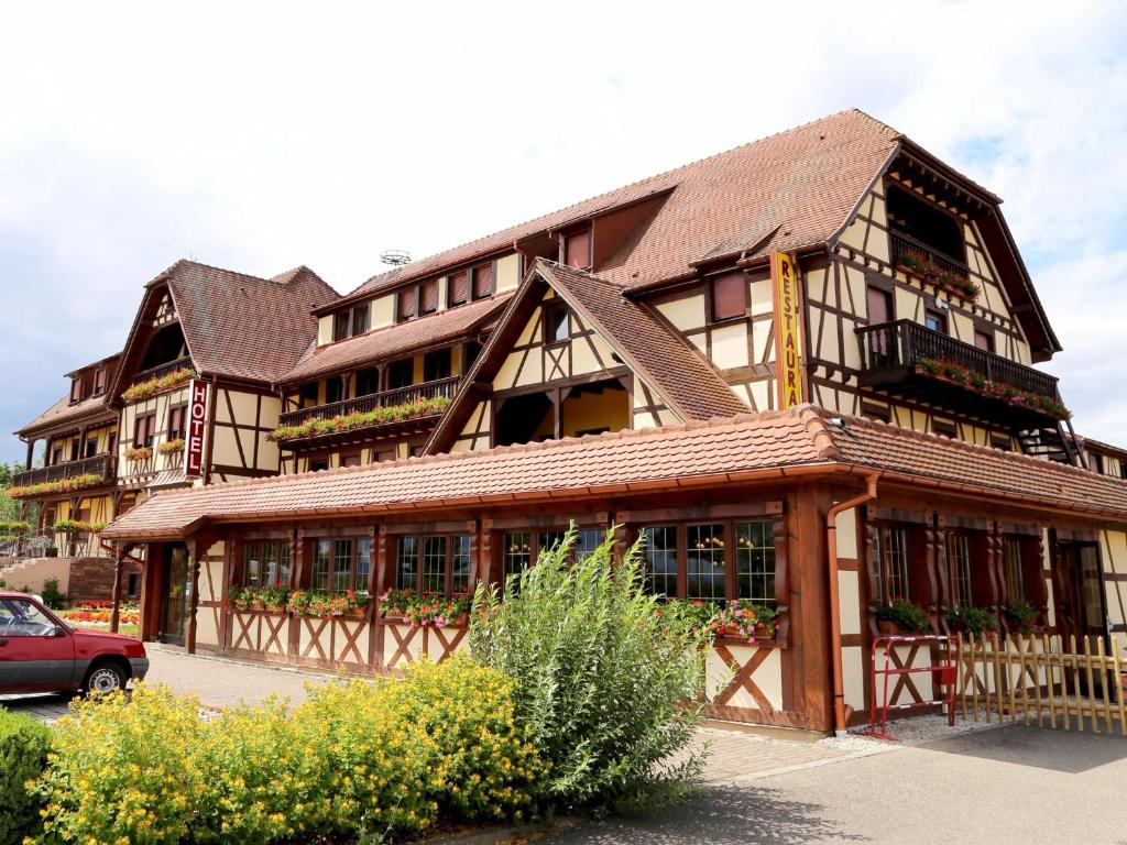 坎特赞Hotel Au Parc des Cigognes的一座大型木制建筑,前面设有停车场