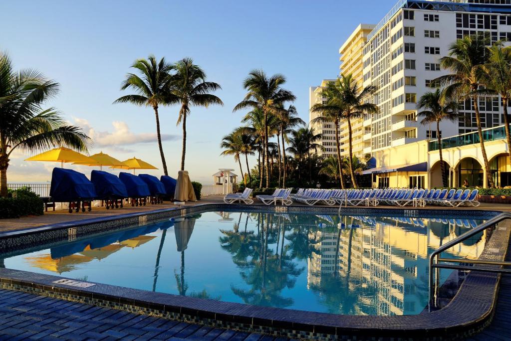 劳德代尔堡海天度假酒店的一座带椅子和棕榈树的游泳池以及一座建筑