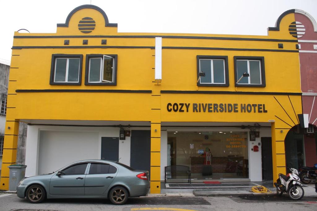 马六甲Cozy Riverside Hotel的停在黄色建筑前面的汽车