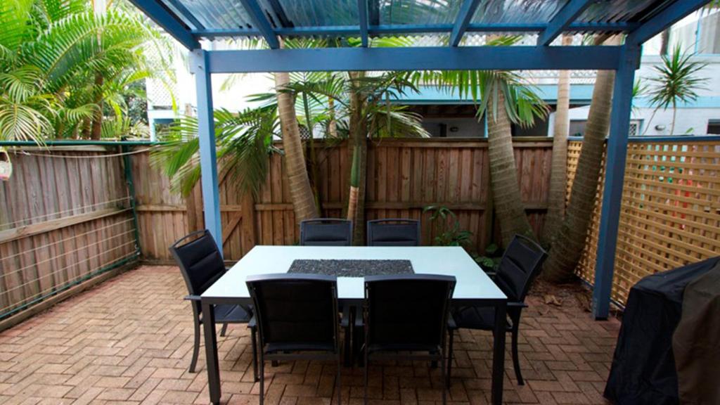 拜伦湾Byron Bay Accom Unit 3 41 Childe Street - Belongil Beach Apartment的棕榈树庭院内的桌椅