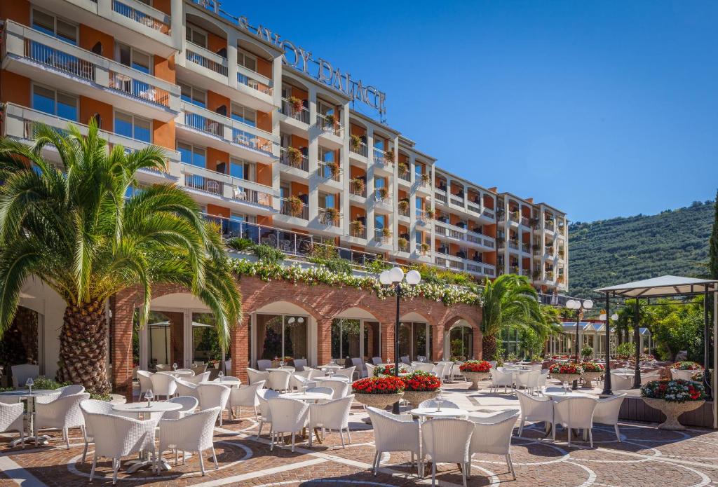 加尔达湖滨托奈利萨伏依皇宫酒店的酒店庭院设有桌椅,棕榈树