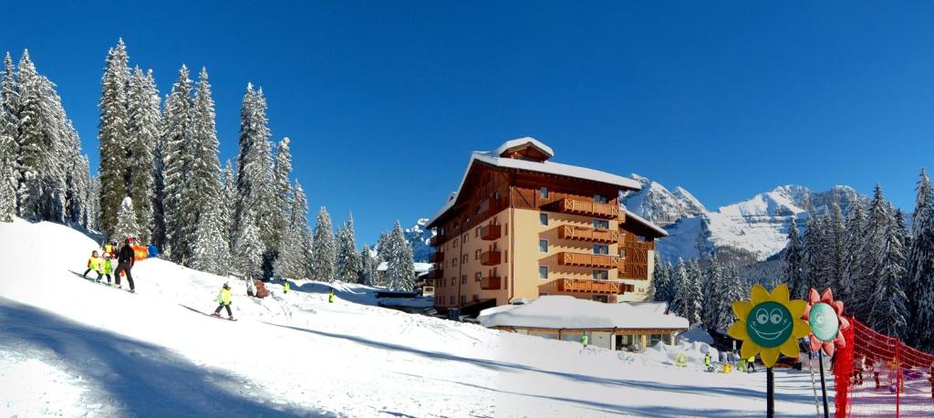 摩德纳迪-坎皮格里奥卡罗芒果温泉假日酒店的一群人沿着一座大楼旁边的雪覆盖的斜坡滑雪