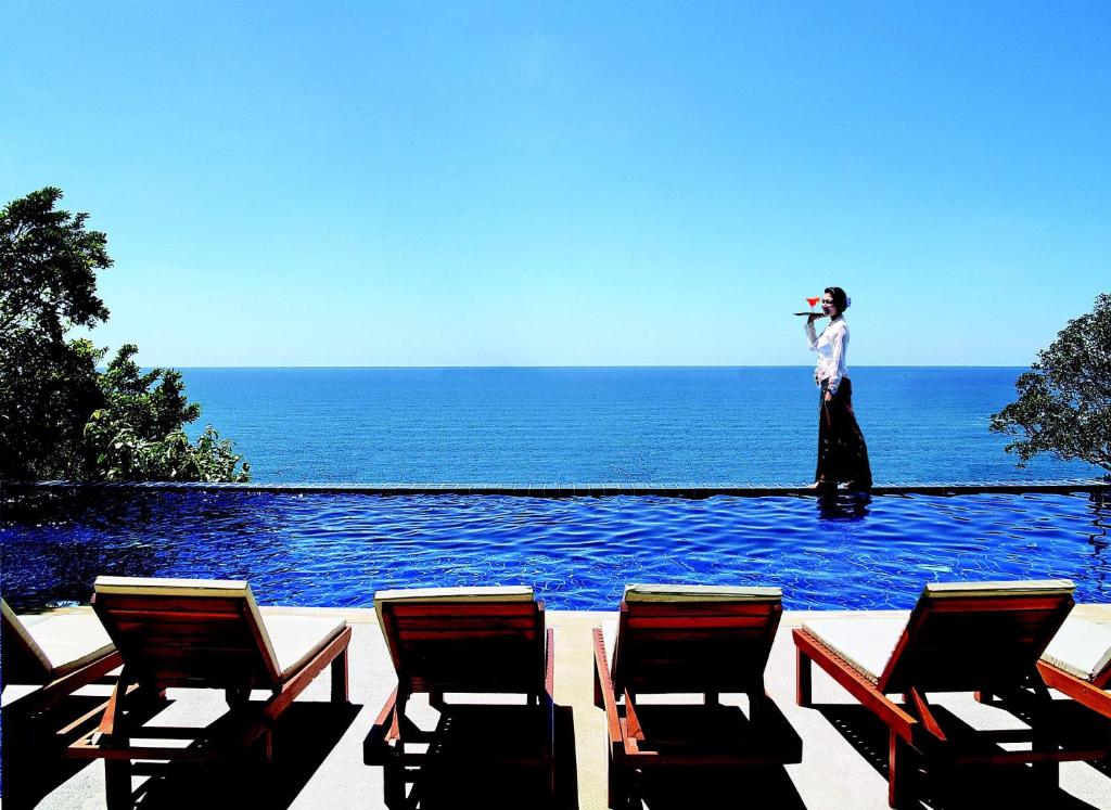 卡伦海滩Secret Cliff Resort & Restaurant - SHA Plus的站在带椅子的游泳池边的女人