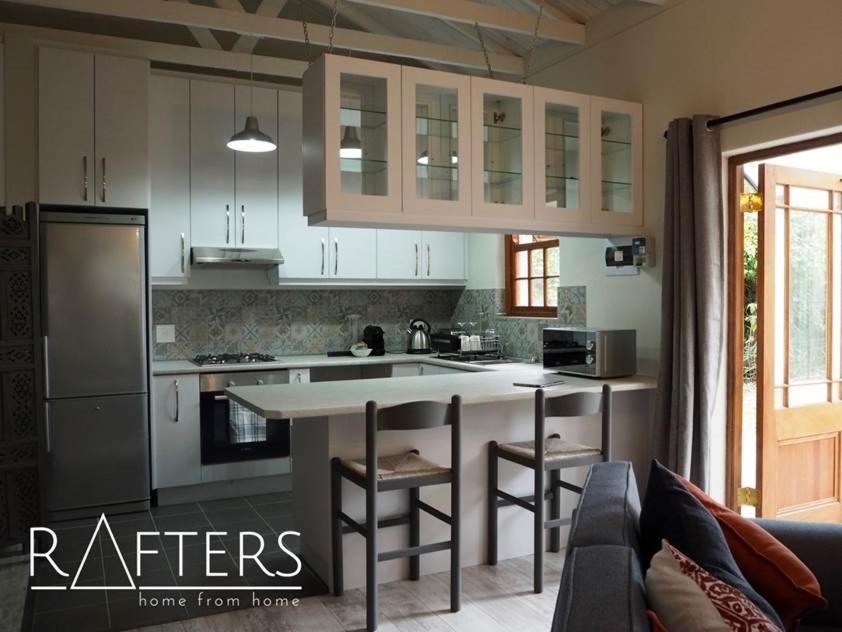 PlumsteadRAFTERS COTTAGE的一间厨房,配有白色橱柜和一个带酒吧凳的厨房岛