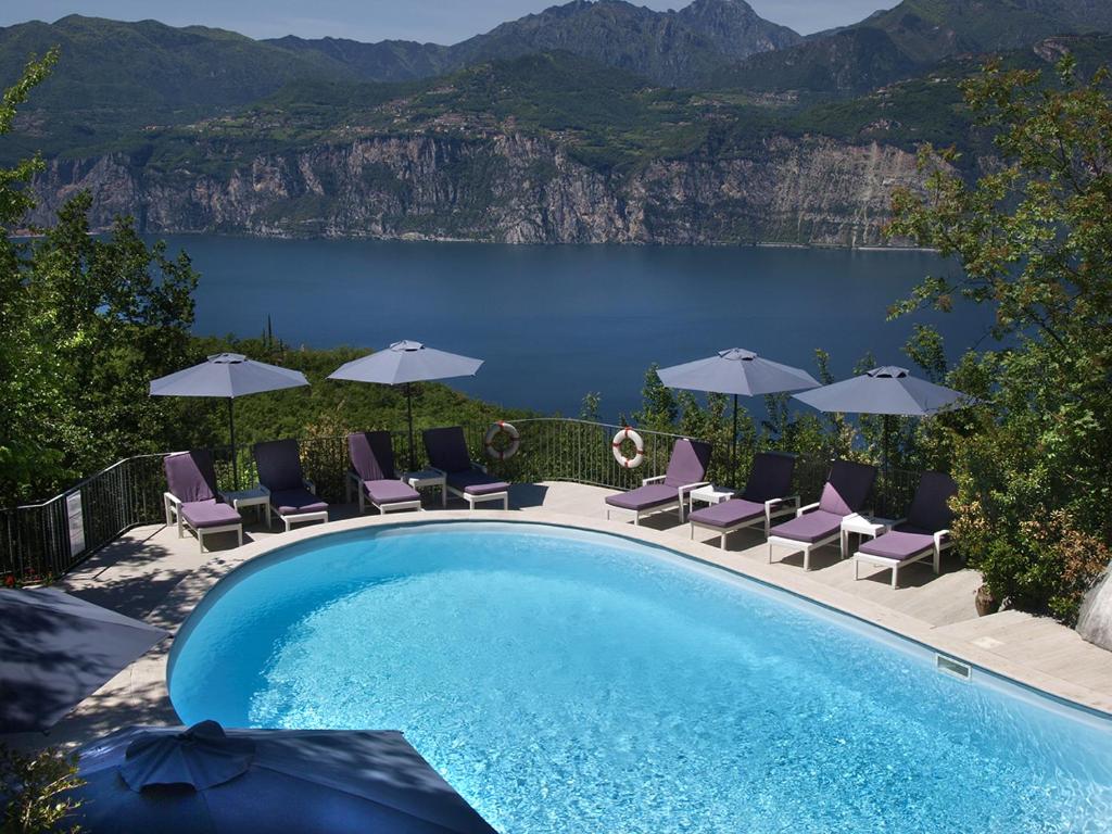 马尔切西内Hotel Querceto Wellness & Spa - Garda Lake Collection的一个带椅子和遮阳伞的游泳池以及一个湖泊