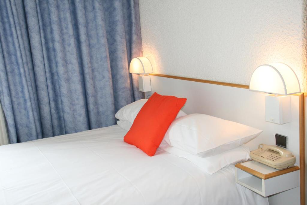 维希Hôtel des Thermes Les Dômes的一张带红色枕头的白色床和一部电话