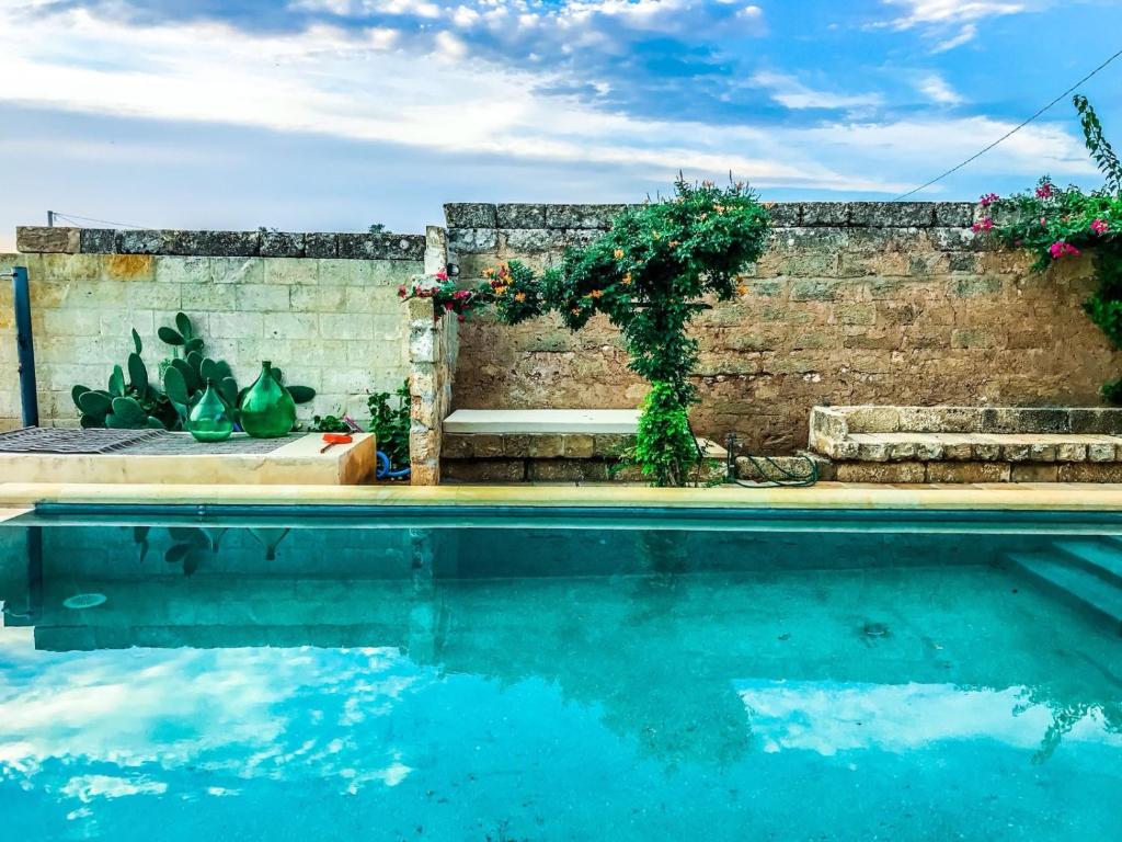 帕拉比塔Masseria Tornesella Don Giuliano的砖墙和一个带长凳及鲜花的游泳池