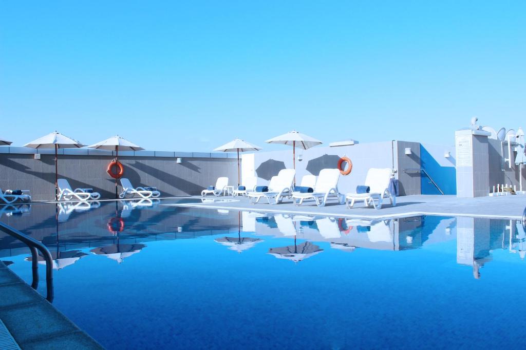 阿布扎比爱迪萨瓦酒店公寓的一个带白色椅子和遮阳伞的游泳池