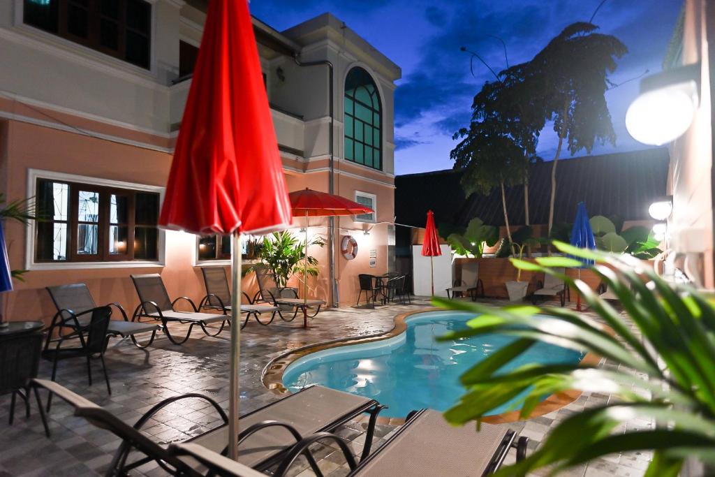 芭东海滩The Villa Residences Resort的一个带游泳池、椅子和红色遮阳伞的庭院