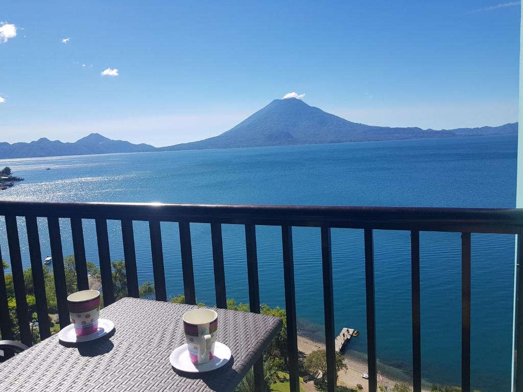 帕纳哈切尔Sky view Atitlán lake suites ,una inmejorable vista apto privado dentro del lujoso hotel的阳台顶部的桌子上放着两杯,俯瞰水面