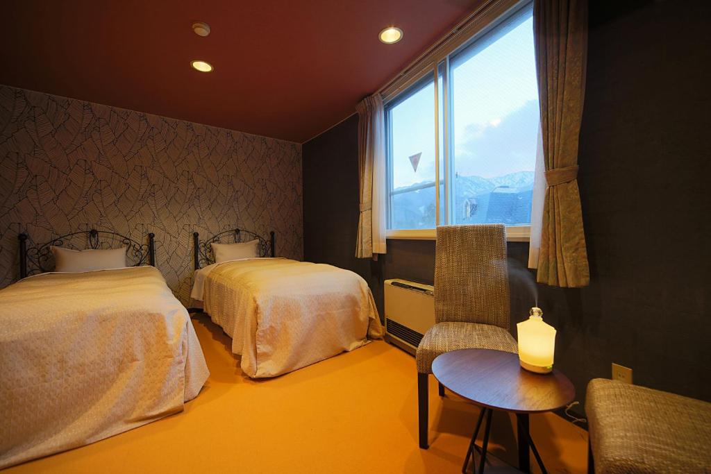 白马村HOTEL 24sweets HAKUBA的一间卧室设有两张床、一把椅子和一个窗户。