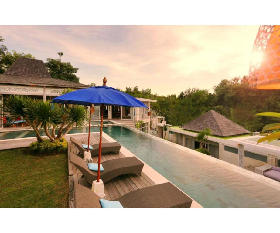 乌鲁瓦图乌鲁瓦图日落天堂别墅的一座房子旁的游泳池,配有蓝色遮阳伞和长椅
