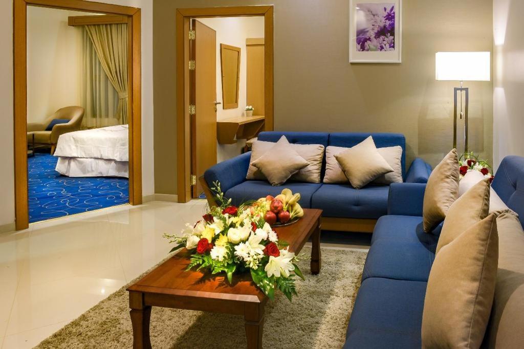 哈萨Fiori Hotel Suites的客厅配有蓝色的沙发和带鲜花的桌子