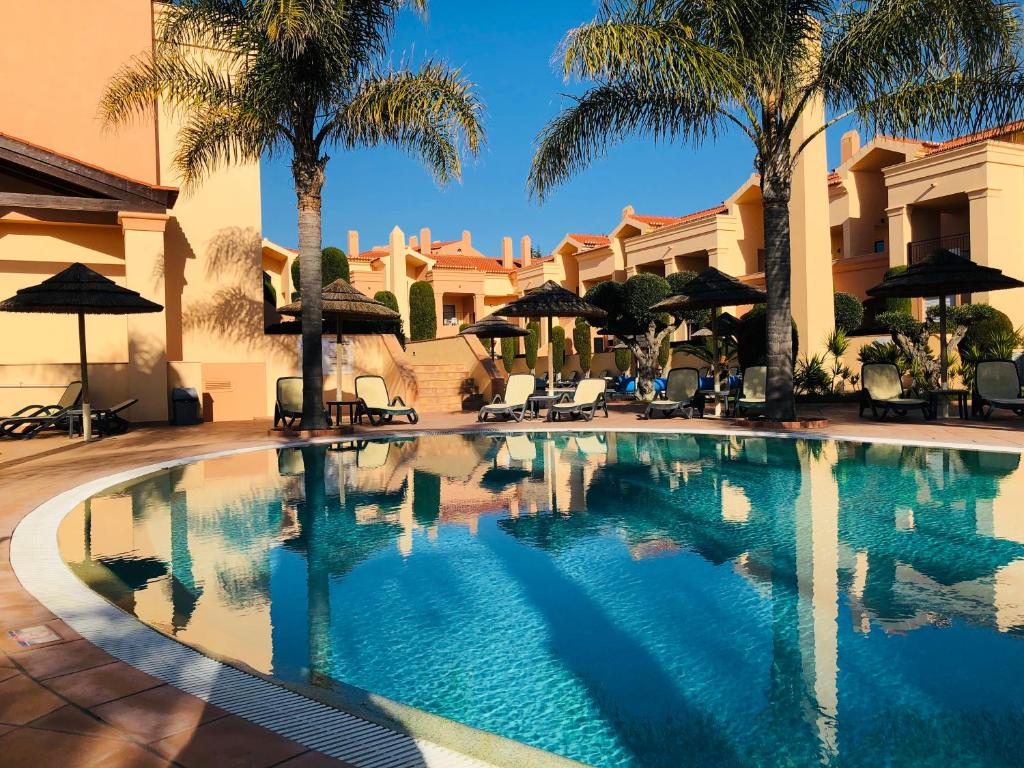 卢斯Luxury Apartment in Praia da Luz的棕榈树和遮阳伞度假村内的游泳池