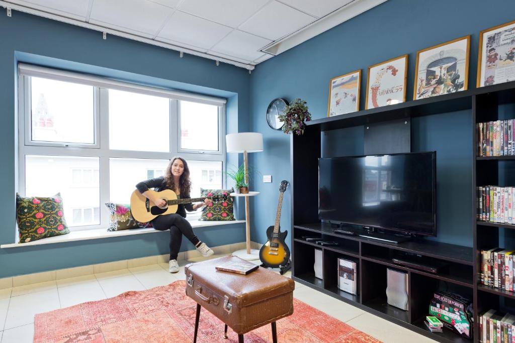 都柏林Canbe Garden Lane Backpackers的坐在窗台上,在客厅里弹吉他的妇女