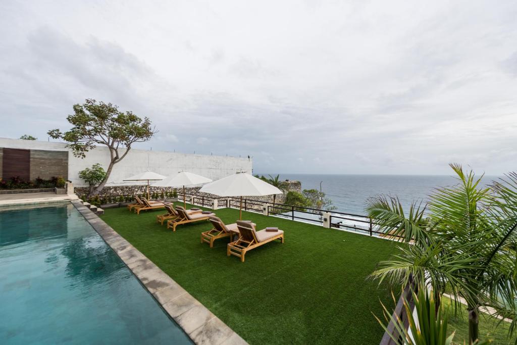 乌鲁瓦图Villa Maiara的毗邻大海的带椅子和遮阳伞的游泳池