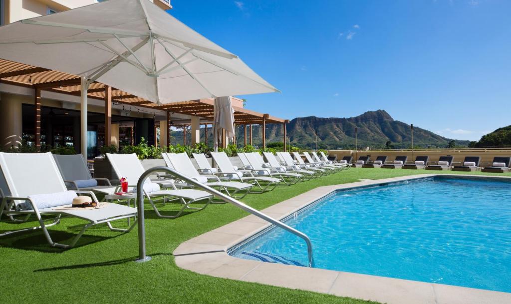 檀香山卡皮欧拉尼皇后酒店的游泳池旁的一排椅子和一把遮阳伞