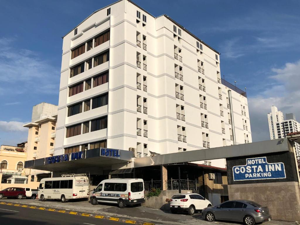 巴拿马城哥斯达旅馆酒店的一座白色的大建筑,前面有汽车停放