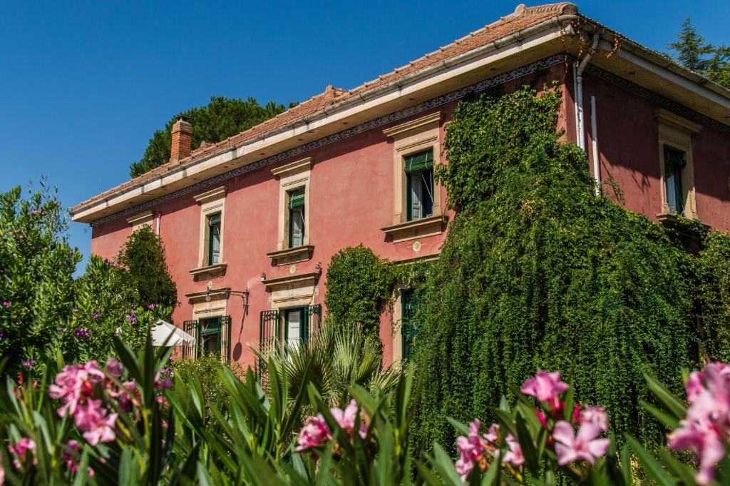 卡尔塔吉罗Affascinante Villa Ottocentesca a Caltagirone的一座常春藤覆盖的建筑,前面有粉红色的花朵
