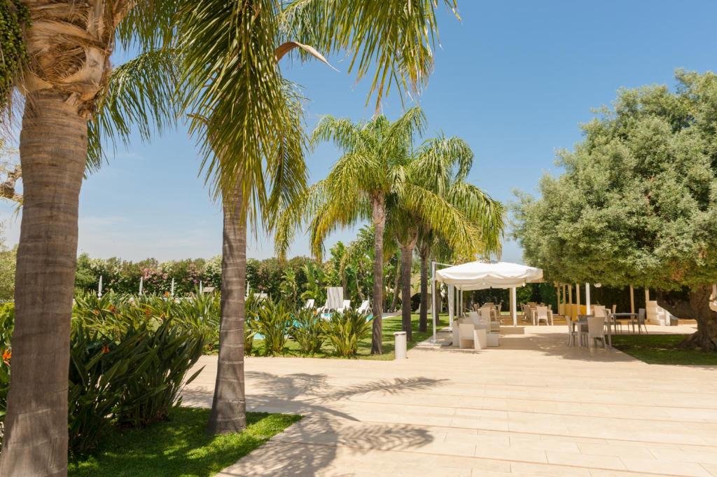锡拉库扎Life Hotels Kalaonda Resort的一座公园,里面种有棕榈树,设有桌子和遮阳伞