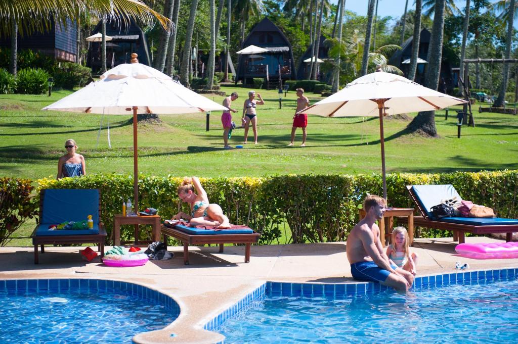 库德岛阁骨岛海滩度假酒店的一群人坐在游泳池边,拿着遮阳伞