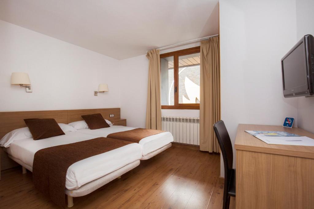 帕斯底拉卡萨Hotel Catalunya Ski的一间卧室配有两张床、一张桌子和一台电视。
