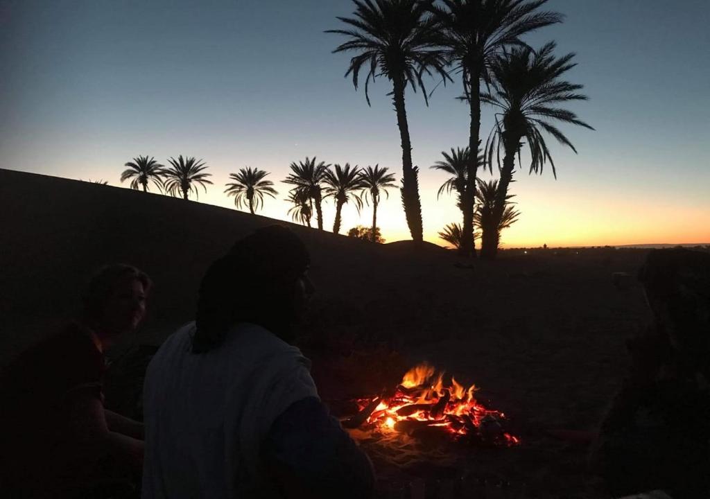 姆哈米德Auberge L'oasis Mhamid的一群人坐在棕榈树的 ⁇ 火旁