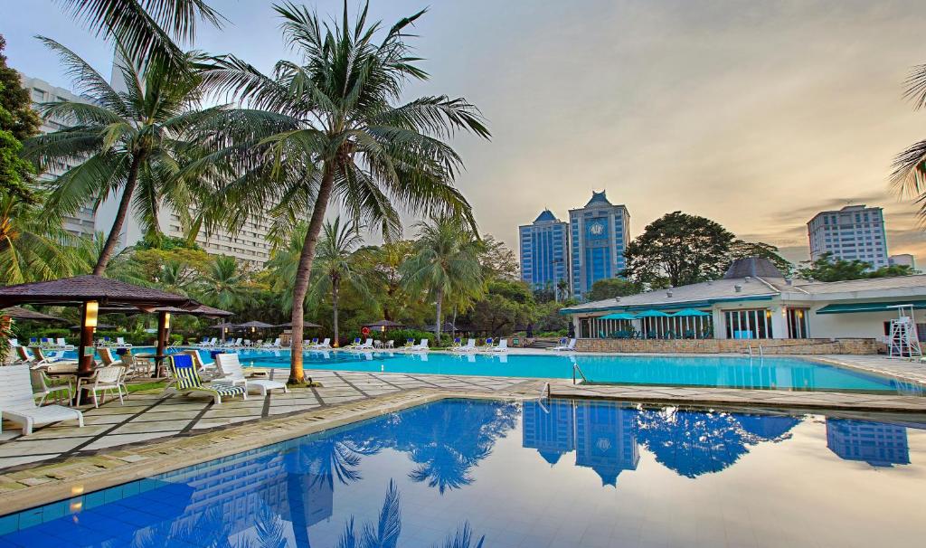雅加达雅加达普罗福圖酒店的一个带椅子和棕榈树的游泳池,以及建筑