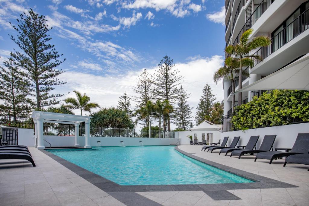 黄金海岸库伦加塔海滩曼特拉酒店的一座游泳池,位于一座带椅子和树木的建筑中