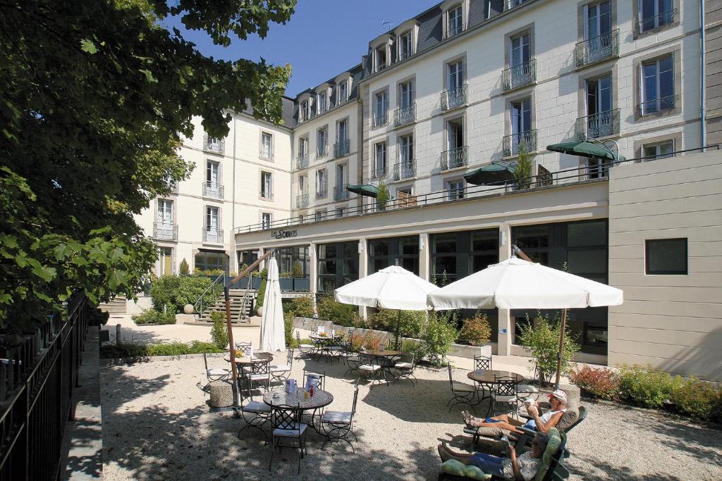 吕克瑟伊莱班HOTEL CERISE - LES SOURCES Luxeuil-les-Bains的大楼前带桌子和遮阳伞的天井