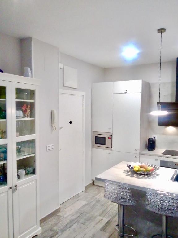 马德里Apartamento estilo nórdico en Malasaña (Madrid Centro)的厨房配有白色橱柜和一张摆着一碗水果的桌子
