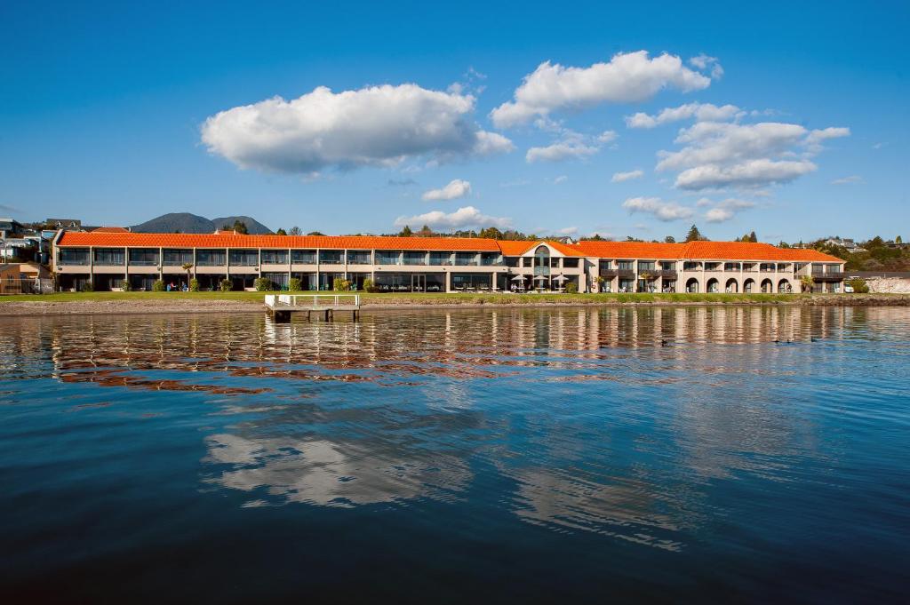 陶波曼努尔陶坡千禧度假酒店的一座有橙色屋顶的建筑,毗邻水体