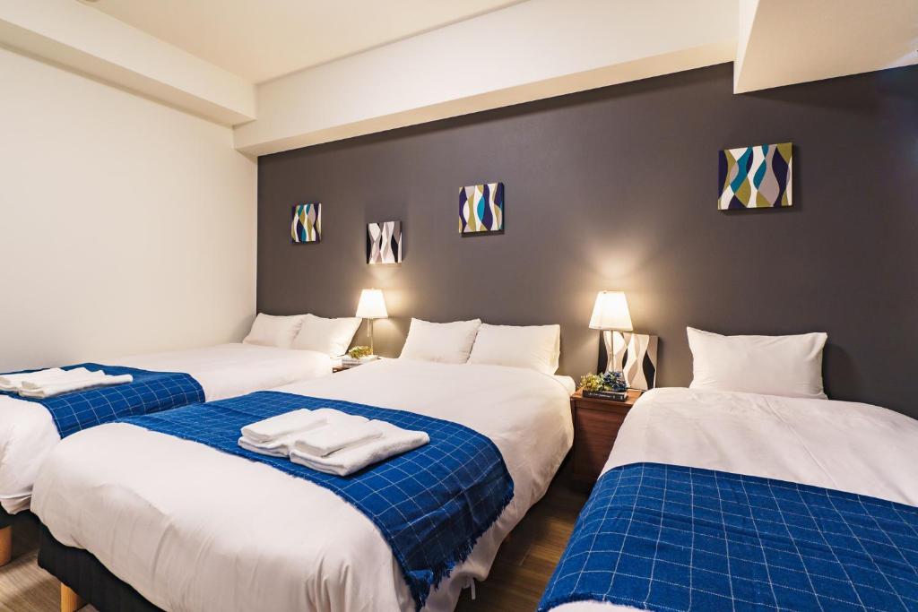 大阪IKIDANE Residential Hotel SHIMANOUCHI的一间设有三张床的客房,配有蓝色和白色的床单