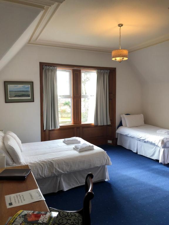 奈恩Westerlea Hotel Nairn的酒店客房设有两张床、一张书桌和一个窗户。
