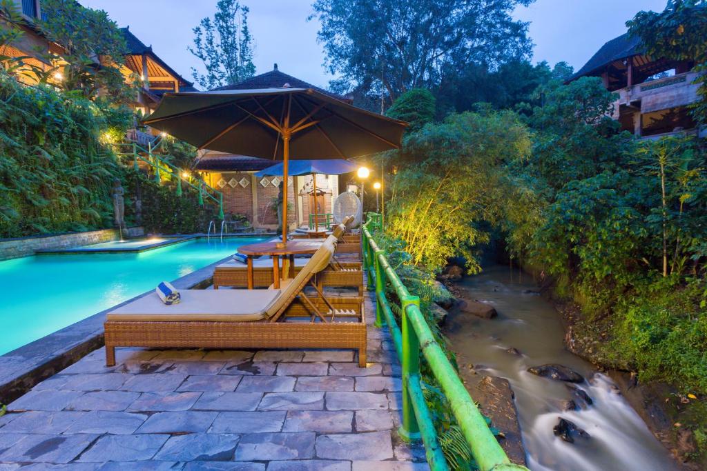 乌布安伊斯别墅的河畔的游泳池配有桌子和遮阳伞