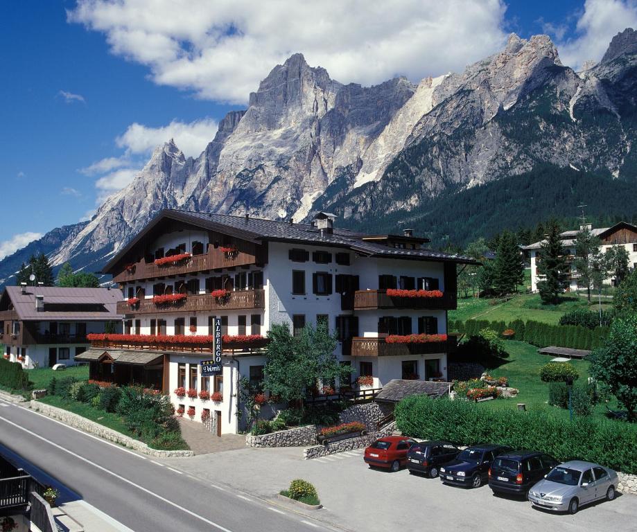 圣维托-迪卡多雷Hotel Albergo Dolomiti的山前有车辆停放的建筑物