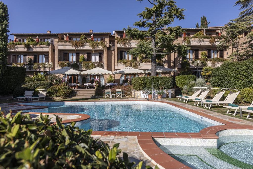 圣吉米纳诺Relais Santa Chiara Hotel - Tuscany Charme的一座游泳池位于酒店前,设有椅子和一座建筑