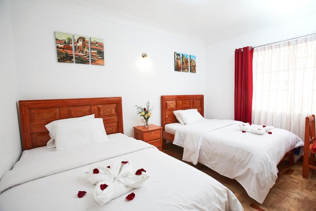 库斯科Hostal Danna Inn的配有两张床铺的房间,上面有白色的床单和鲜花