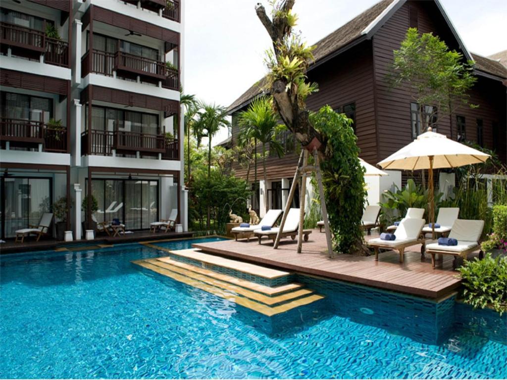 清迈拉林金达温泉度假酒店的一座带椅子和遮阳伞的游泳池位于大楼旁