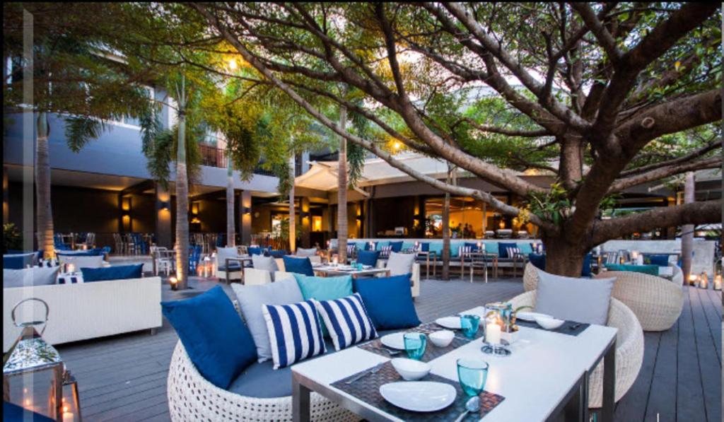 芭堤雅市中心The Leela Resort & Spa Pattaya的一间设有桌椅的餐厅,还有一棵树