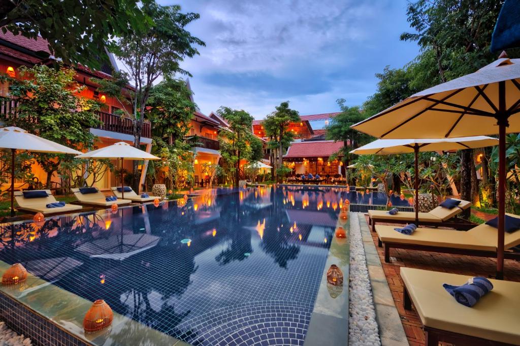 暹粒玛尼村套房酒店的一个带桌子和遮阳伞的酒店游泳池