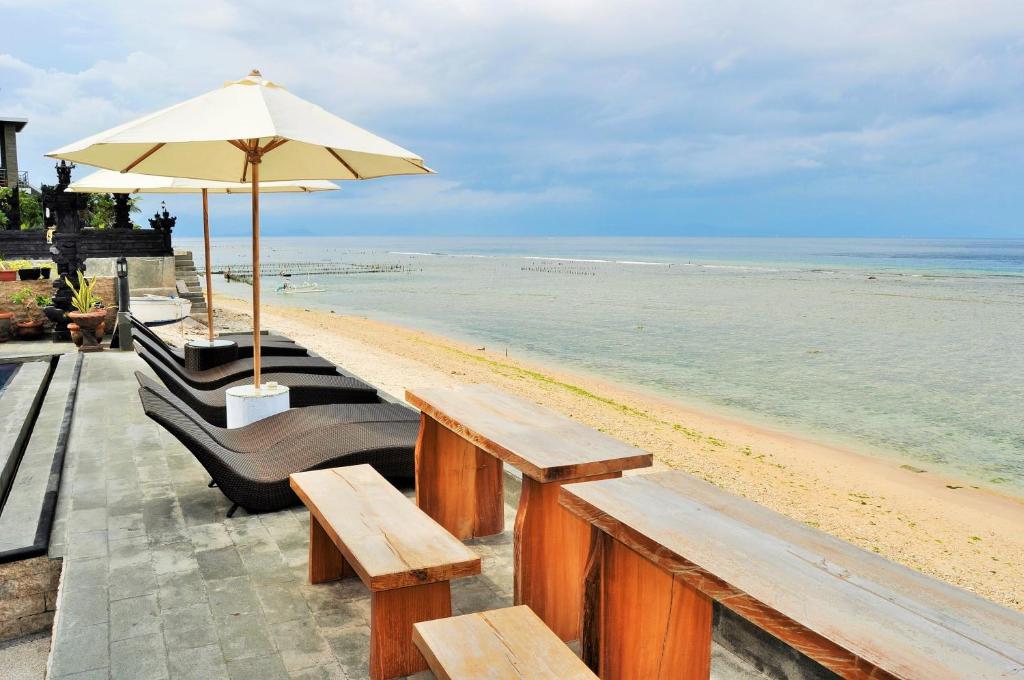 珀尼达岛Pradana Beach Inn Luxury的一个带木长椅和遮阳伞的海滩