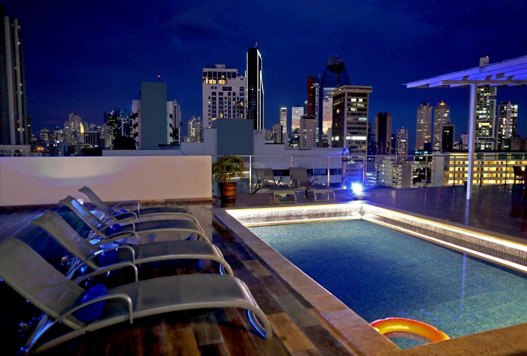 巴拿马城Victoria Hotel and Suites Panama的屋顶游泳池设有椅子,晚上则享有城市天际线