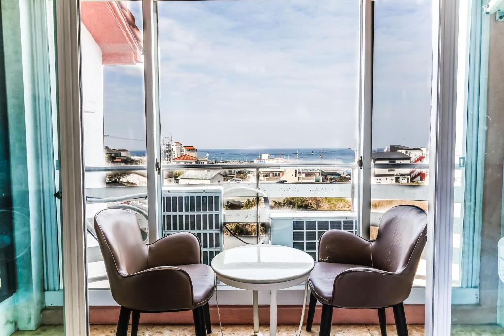 济州市济州海洋家庭酒店的客房设有两把椅子、一张桌子和大窗户