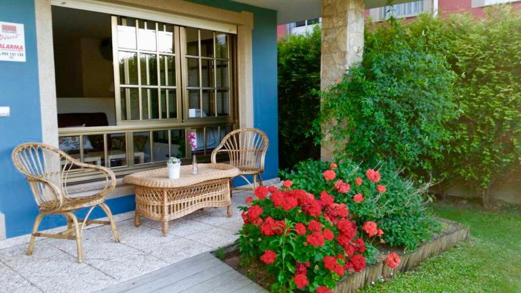 米尼奥Housingcoruña Apartamento Playa Miño 01的庭院配有两把椅子和一张桌子,种有鲜花