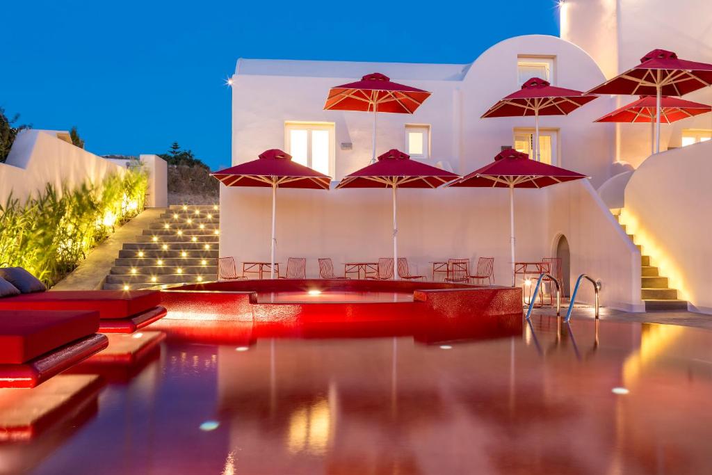 皮尔戈斯圣托里尼艺术酒店的大楼前的带红伞的游泳池