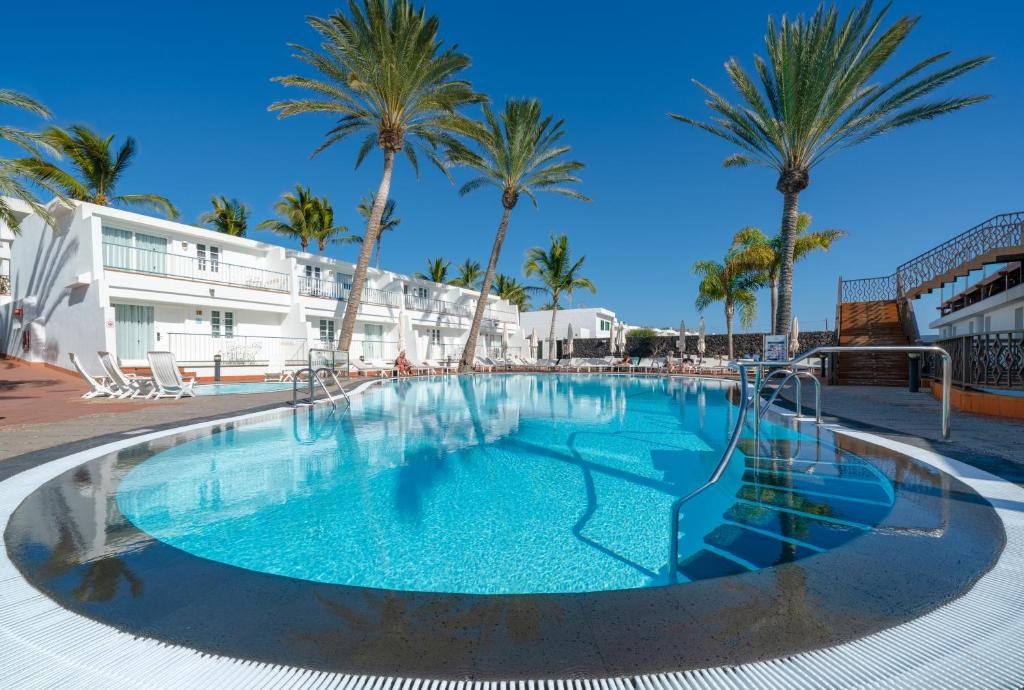 卡门港Plus Fariones Apartamentos的一座大型游泳池,在一座建筑前种有棕榈树