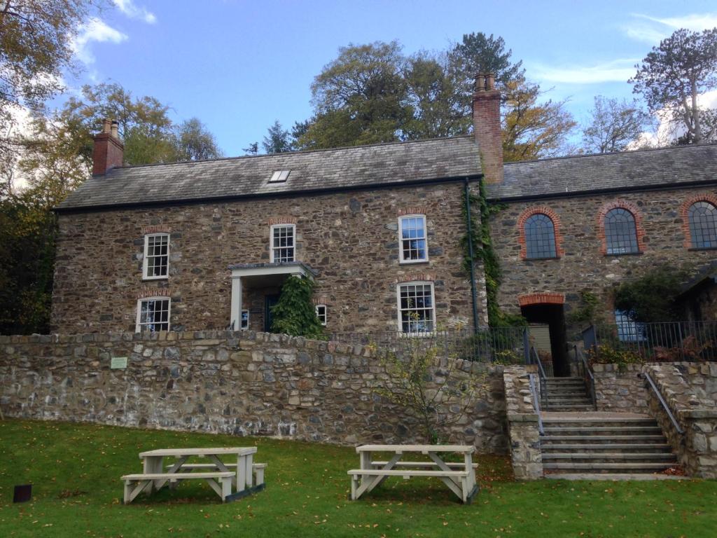 康威The Farmhouse at Bodnant Welsh Food的石头建筑前面设有两张野餐桌