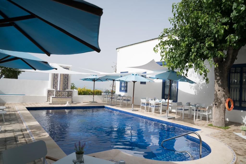 西迪·布·赛义德达累斯萨拉姆酒店的一个带蓝伞和桌椅的游泳池