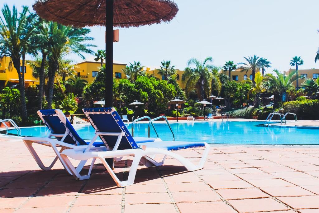 科拉雷侯Oasis Fuerteventura Beach Apartments的游泳池旁的2把躺椅和遮阳伞